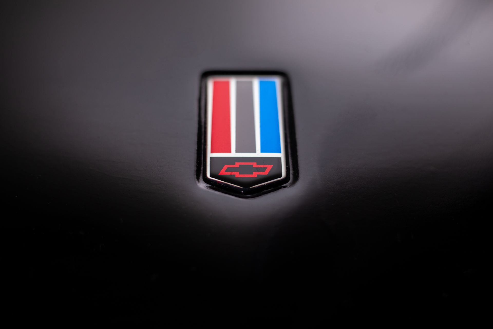 Close-up of a Chevrolet badge. The badge has a red, gray, and blue vertical stripe design over a red bow-tie emblem.