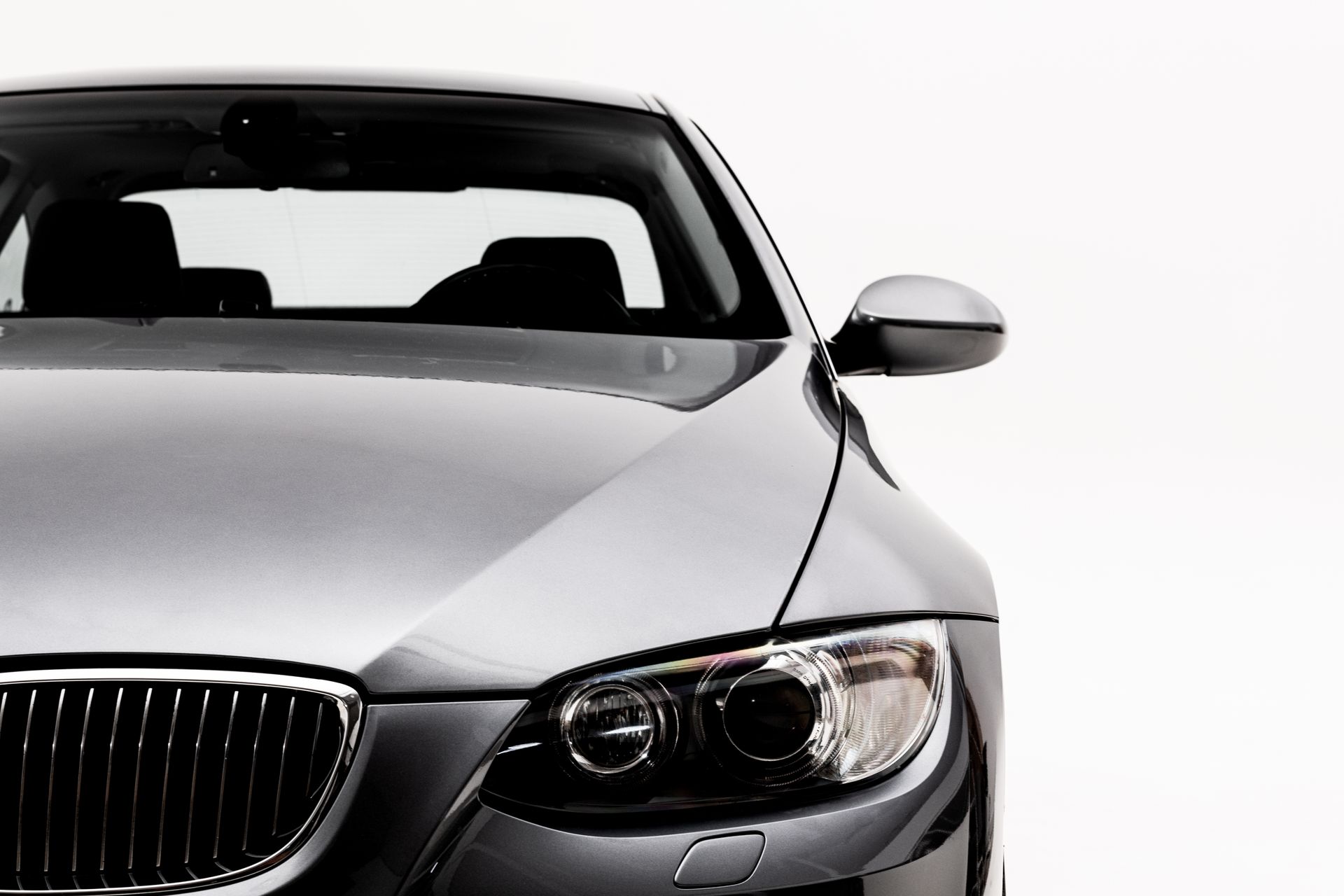 Silver car, partially visible, against a white background; shows front grill, headlight, and side mirror.