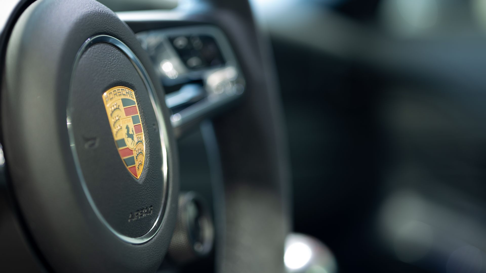 Close-up of a Porsche steering wheel with the brand's crest in the center.