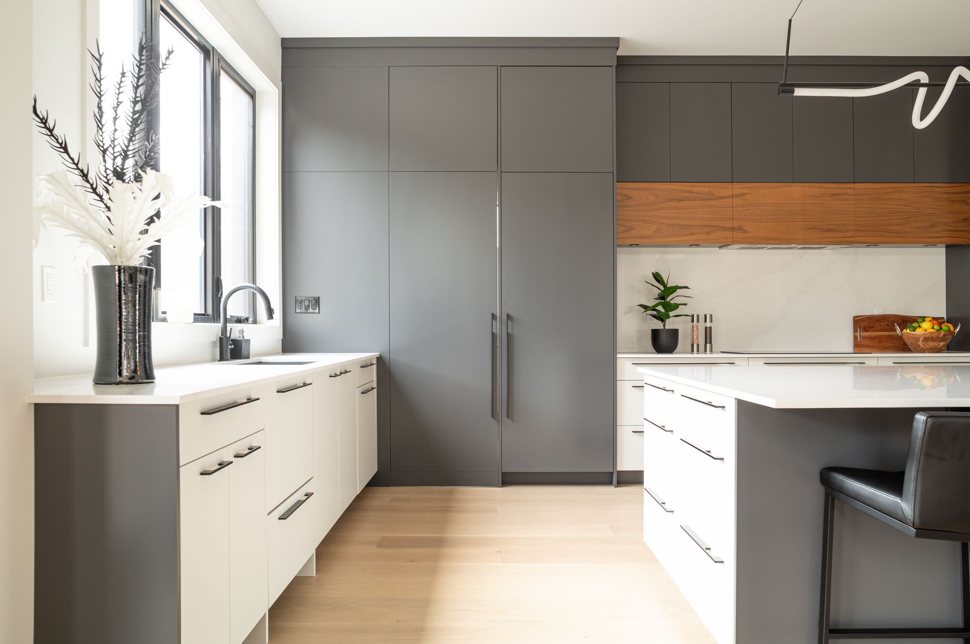 Modern kitchen with gray and white cabinetry, a large window, and light wood flooring.