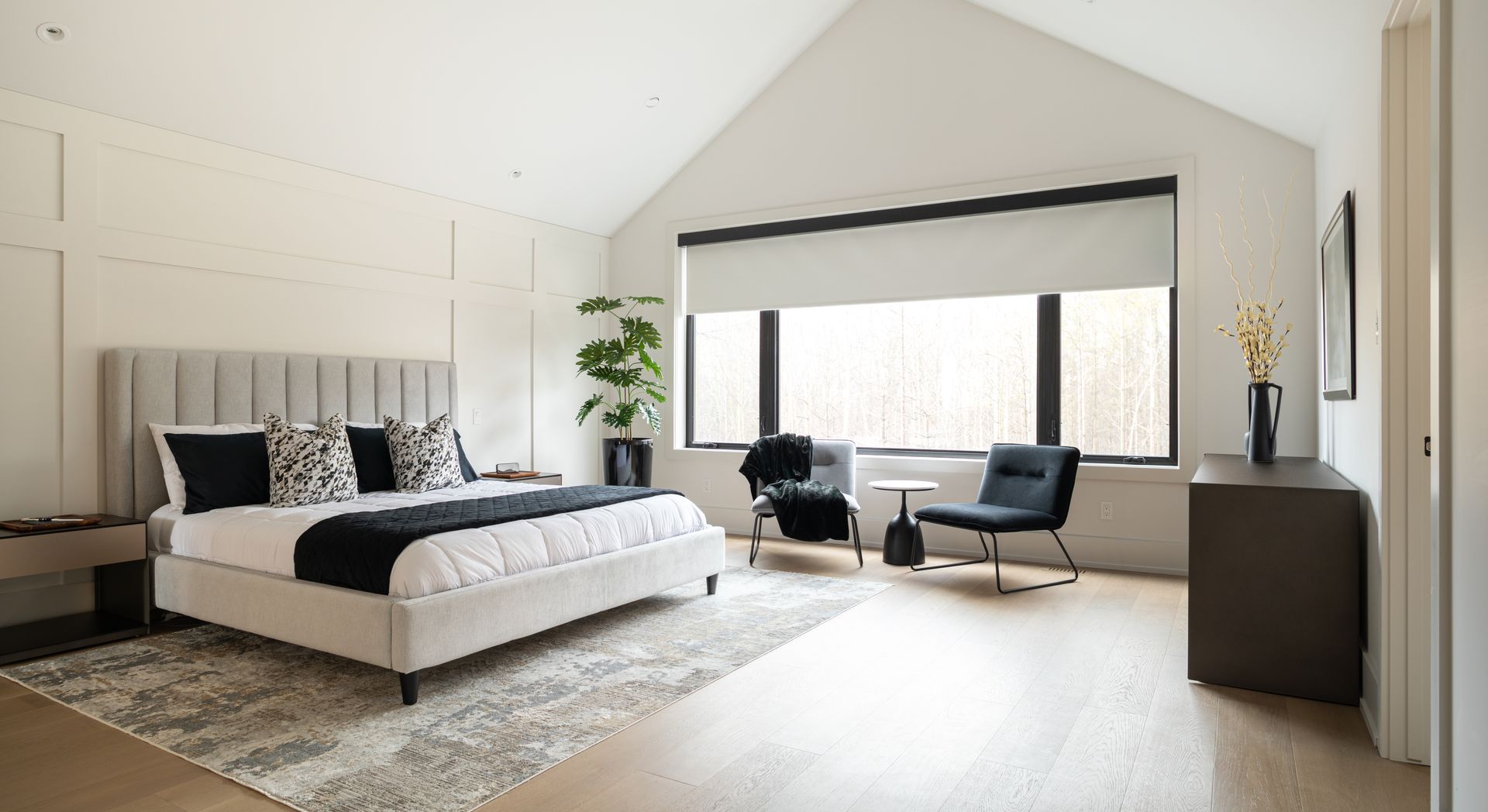 Modern bedroom with bed, chairs, and window with light coming through.