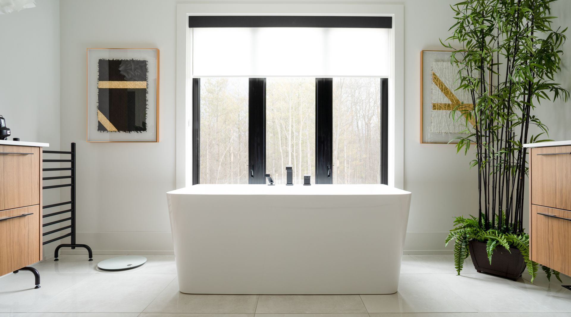 Modern bathroom with white tub, large window, bamboo plant, and light wood vanities.