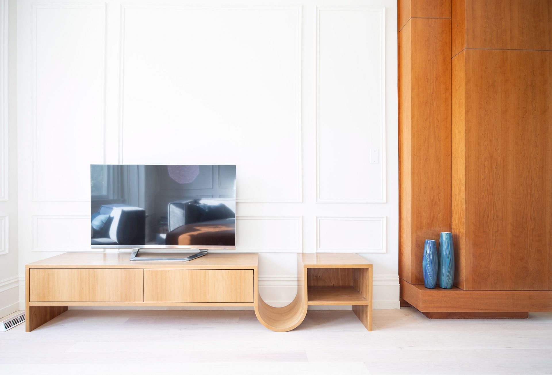 Living room with light wood TV stand, side table, and built-in cabinet against a white paneled wall.