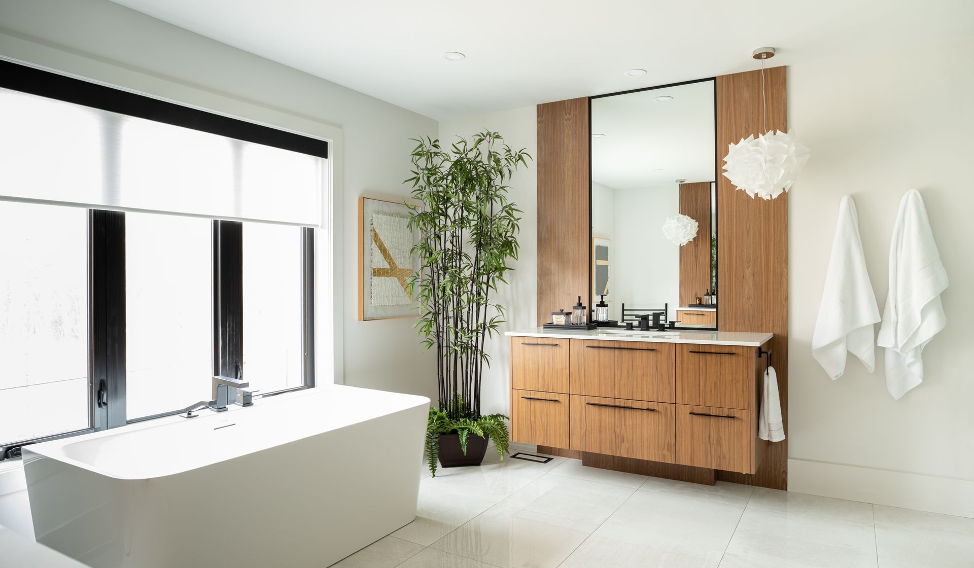 Modern white bathroom with a tub, wooden vanity, large mirror, and plant.