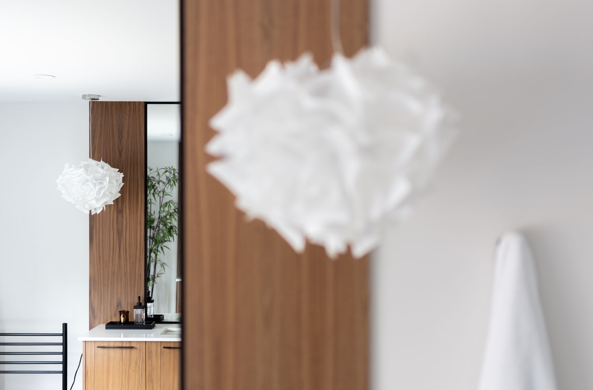 White paper pendant lights hang in a minimalist, light-filled bathroom with wooden cabinetry.