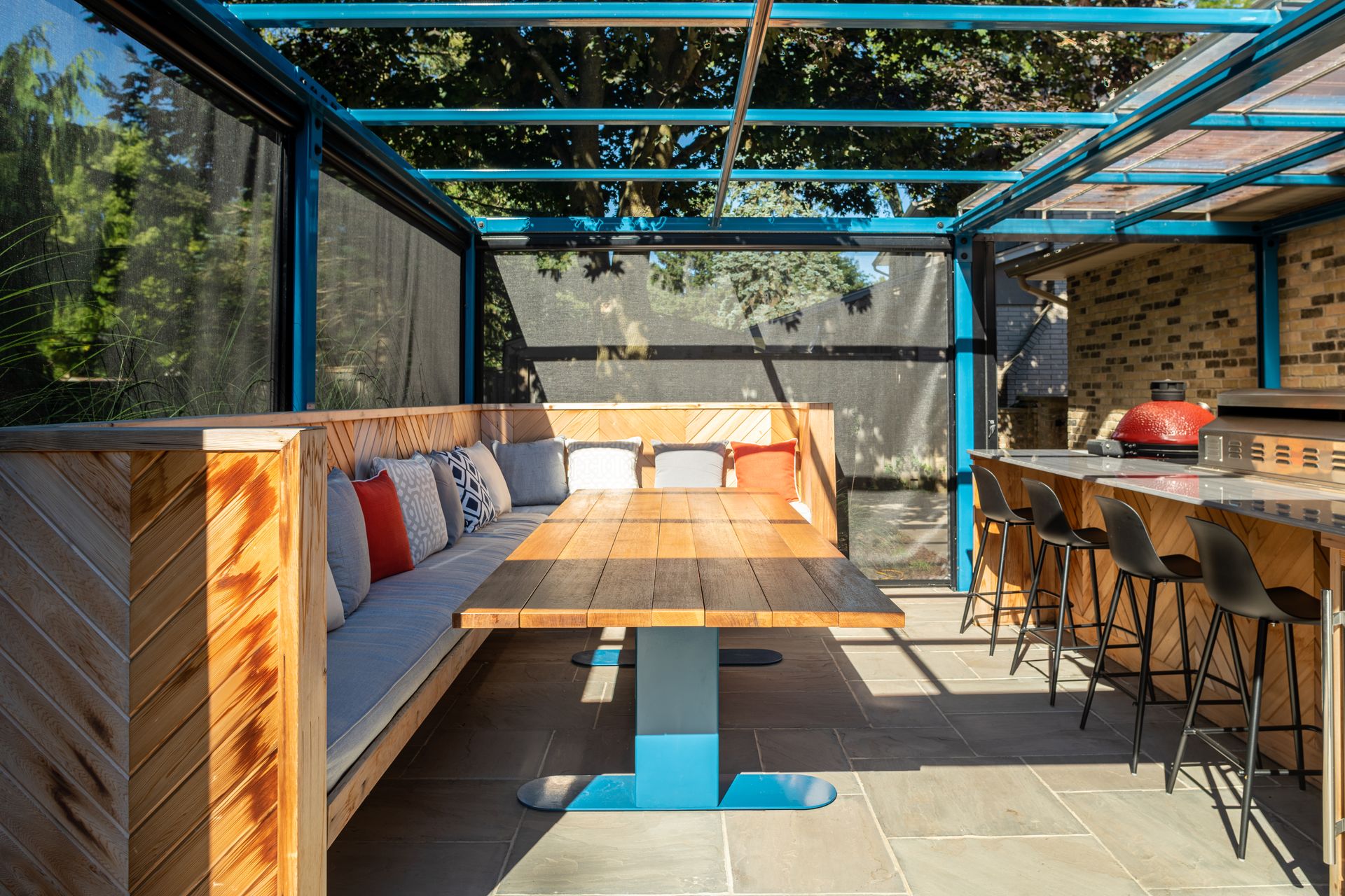 Outdoor dining area with wooden booth, table, and bar stools, under a blue canopy.