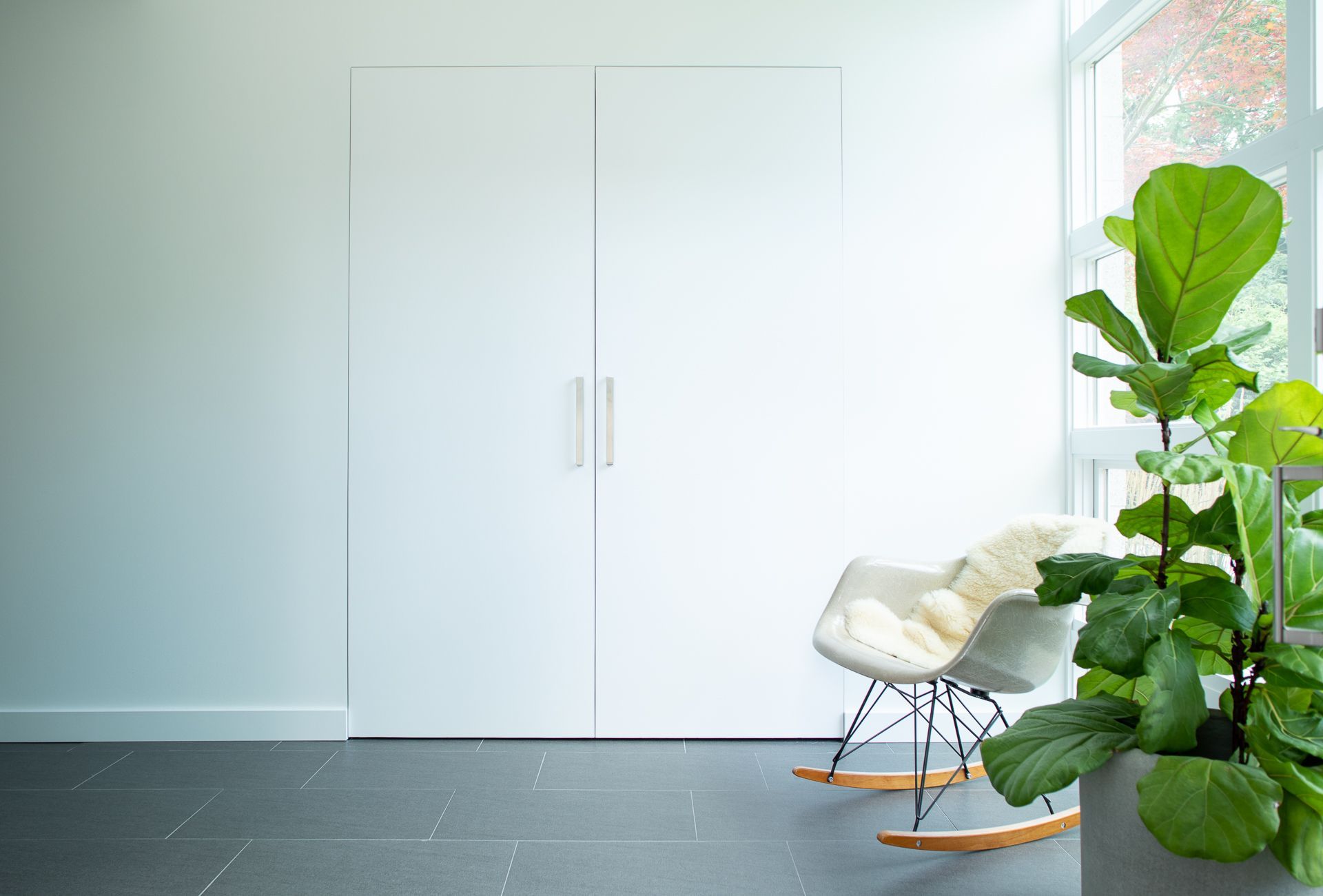 White room with rocking chair, plant, and tall doors.