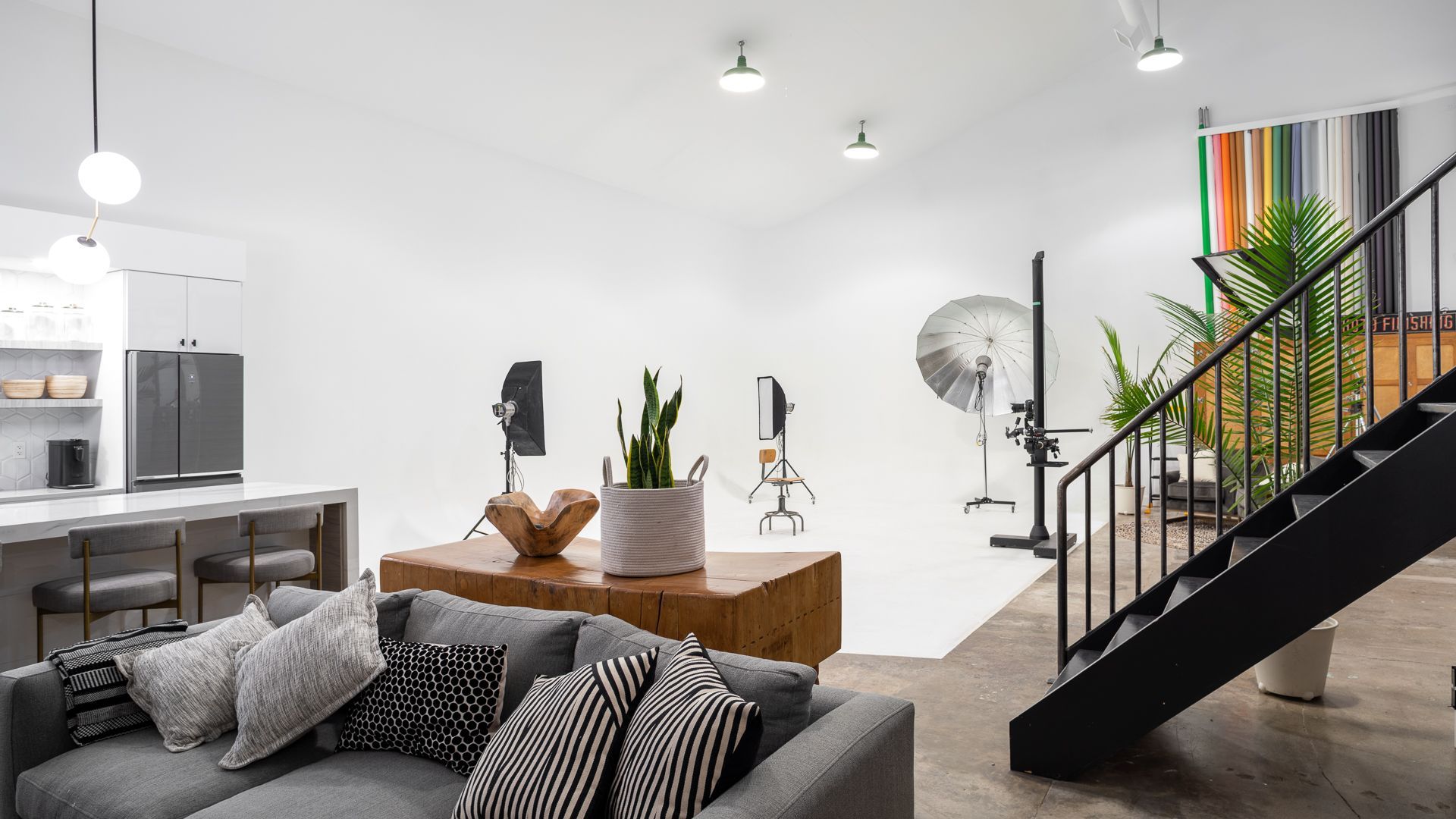 Photo studio with a seating area and white backdrop, various lights, and stairs leading up.