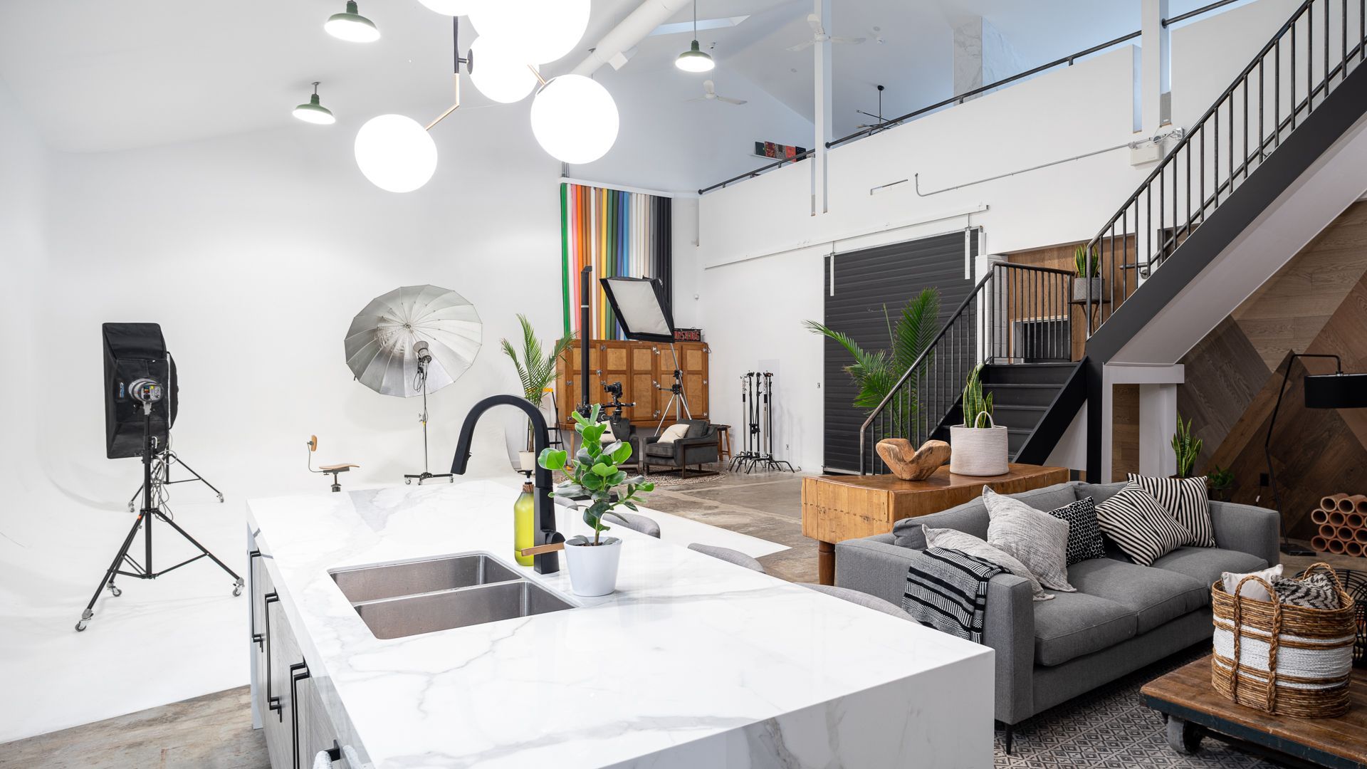 Bright, modern studio kitchen with a white countertop and a gray sofa. Photography equipment is set up.