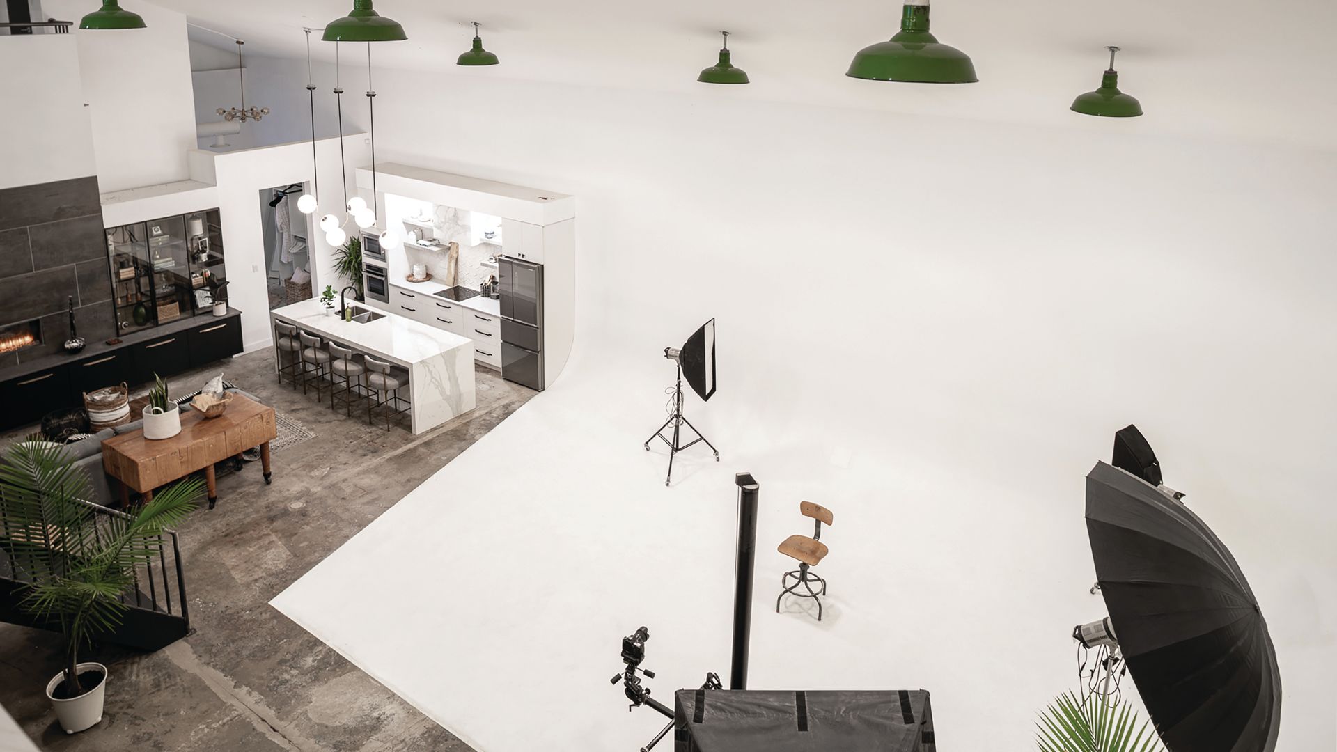 High-angle shot of a bright studio with a kitchen set, photo equipment, and white backdrop. 