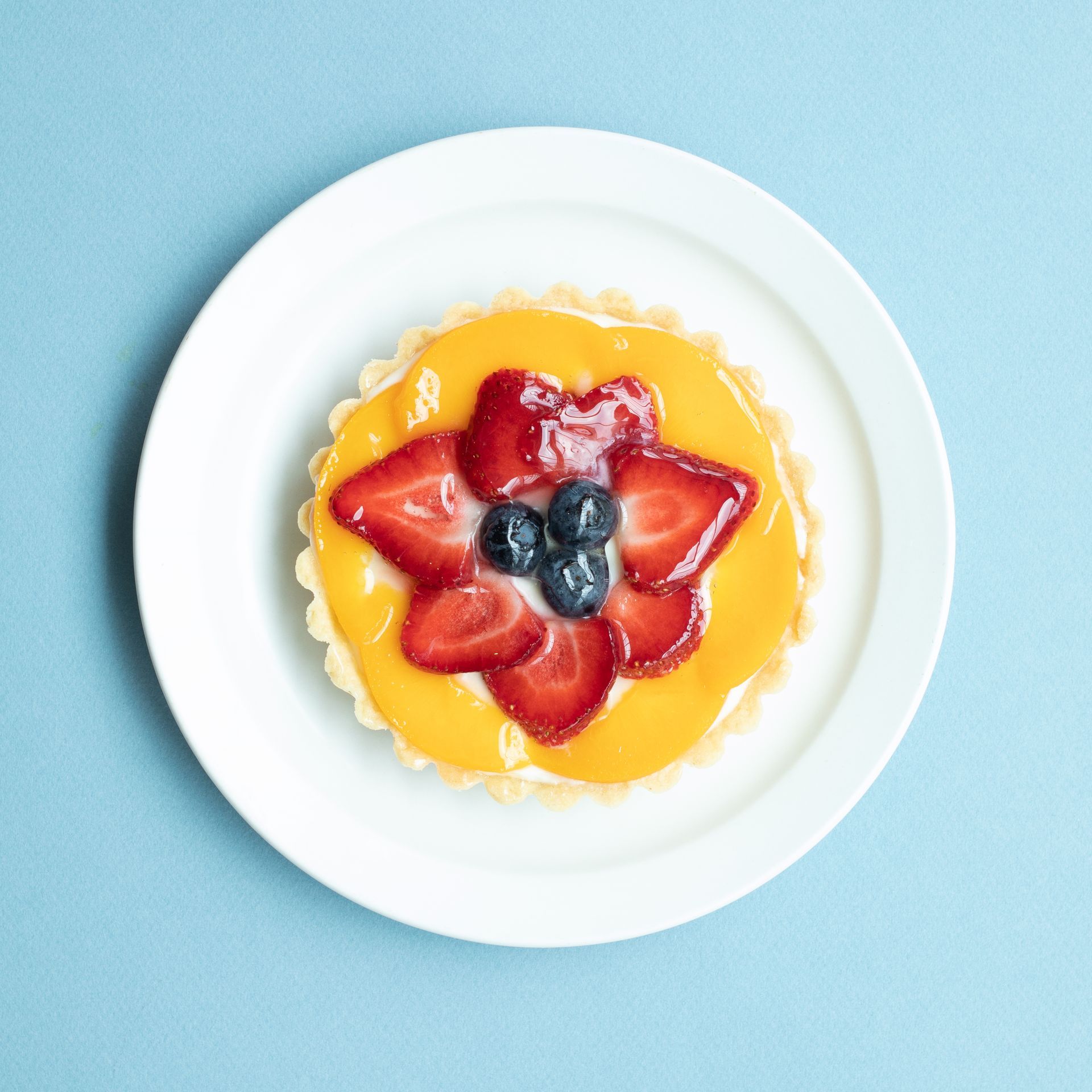 Fruit tart on a white plate: strawberries, blueberries, and yellow glaze over a custard filling.
