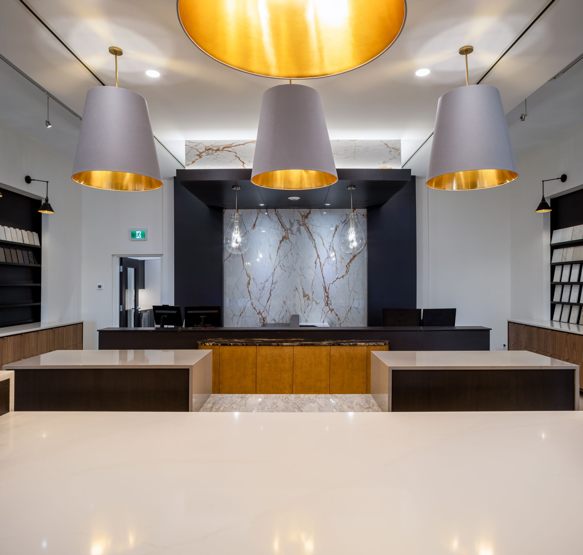 Modern interior with three gray pendant lights over a reception desk with marble backdrop.