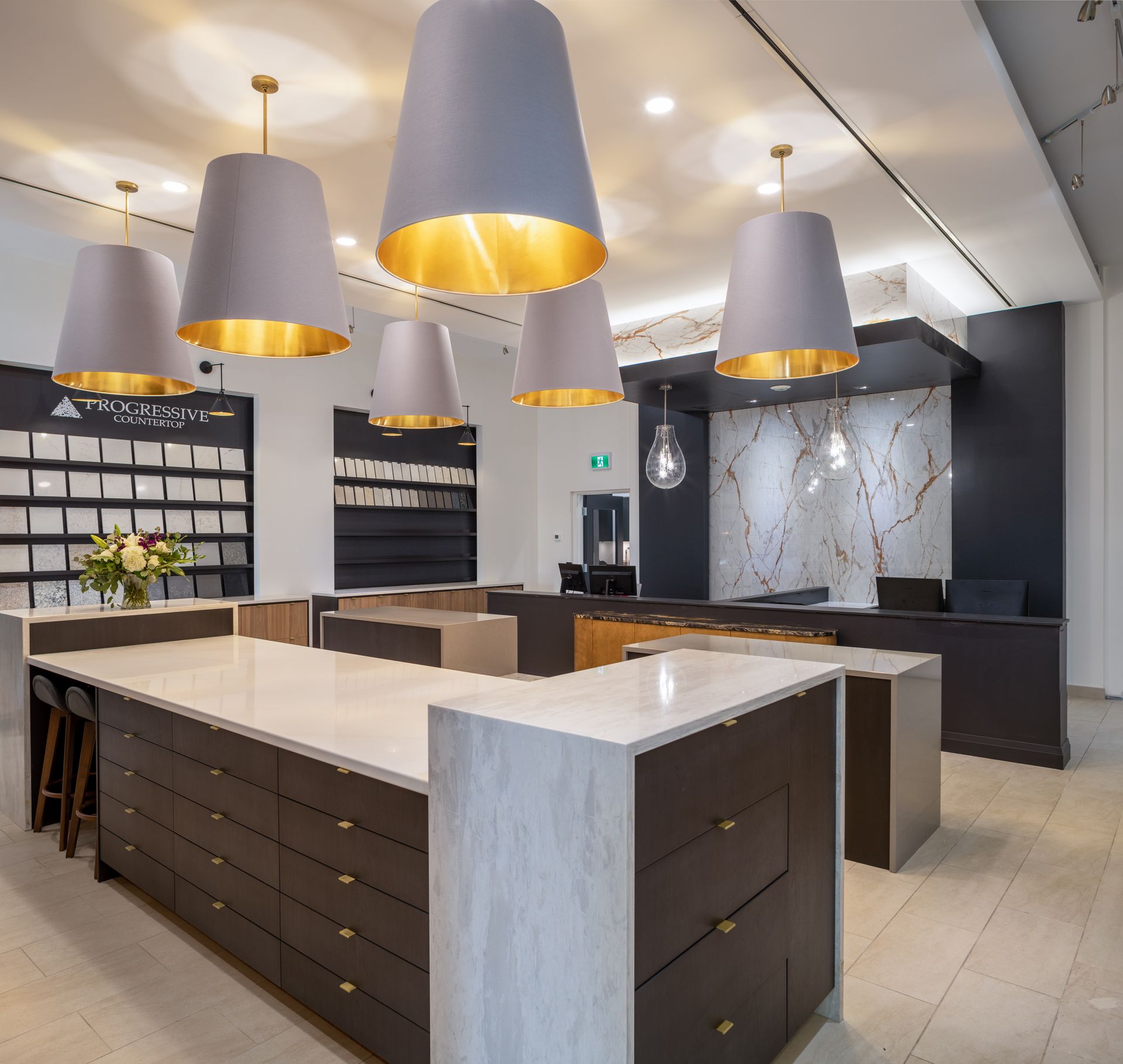 Kitchen showroom with large island, pendant lights, and display of materials.