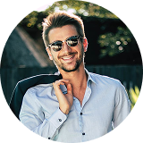 Man wearing sunglasses, smiling, holding blazer, outdoors.
