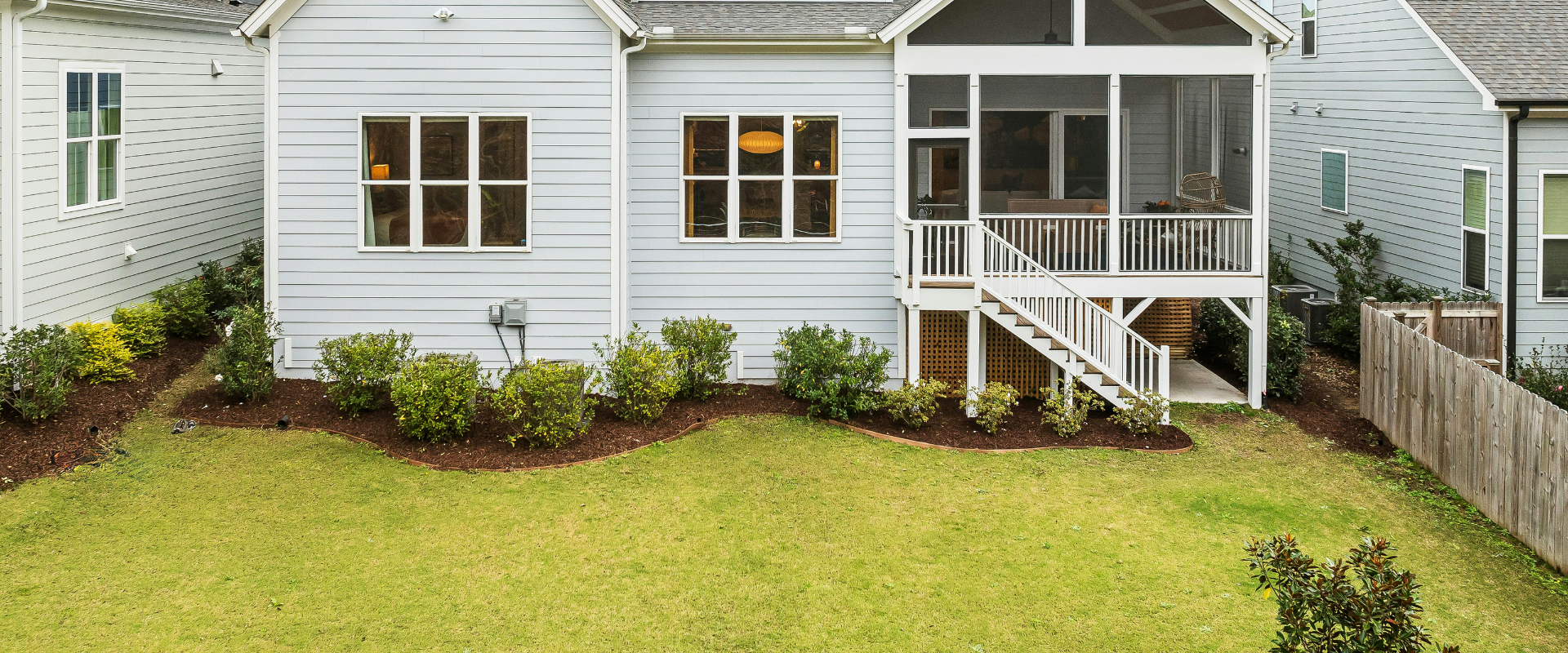Small white house exterior with a grassy backyard and a covered porch with stairs
