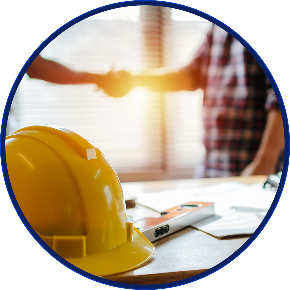 Yellow hard hat, level, and blueprints on table. Blurred figures shaking hands in the background.
