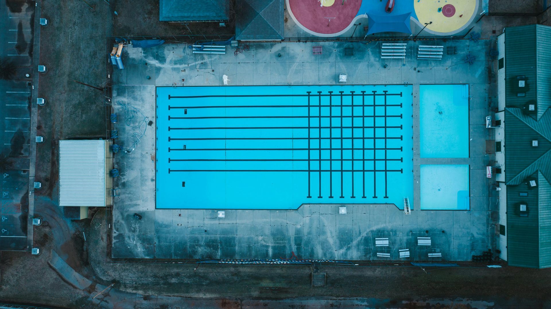 Two professionals in work clothes shake hands over a table with a white hard hat, laptop, and blueprints.