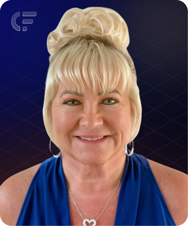 Woman with blonde updo smiles, wearing a blue top and a heart-shaped necklace.