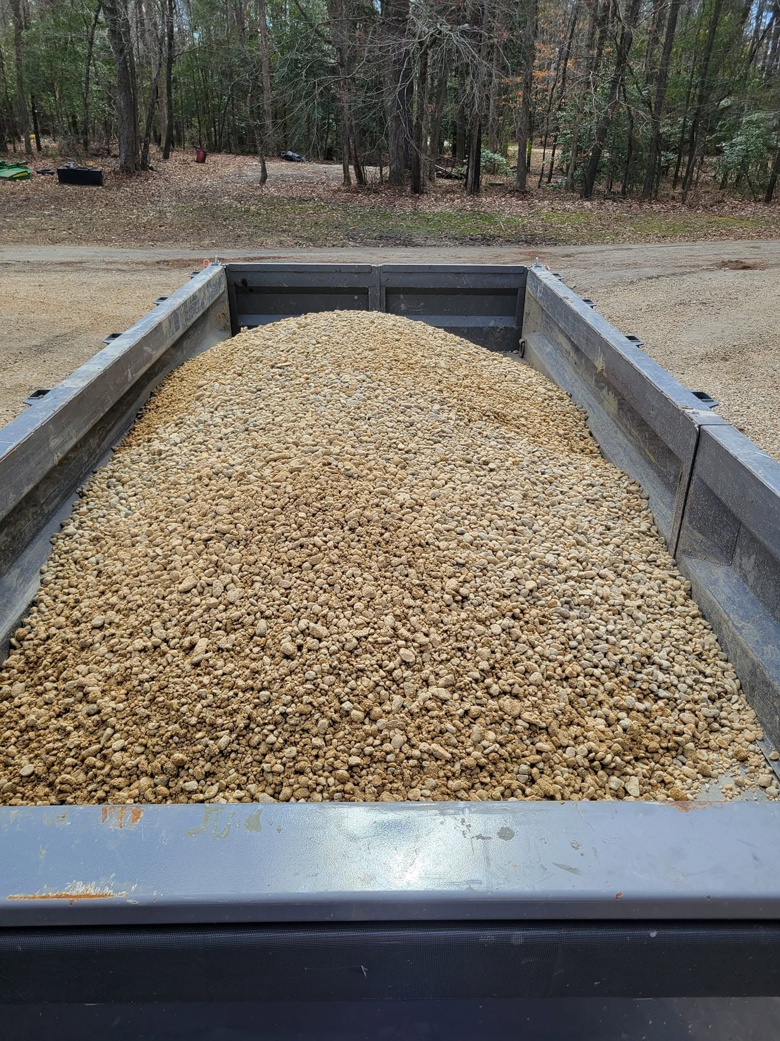 Dump truck bed filled with tan gravel or pea stone at a wooded worksite