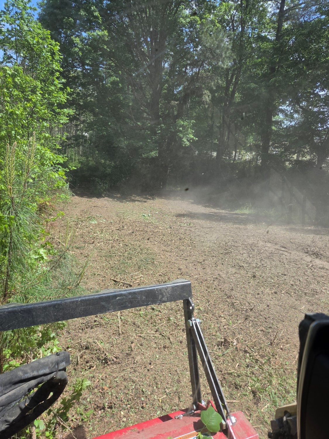 Dusty gravel trail in a wooded area, viewed from a vehicle with metal rails in the foreground.
