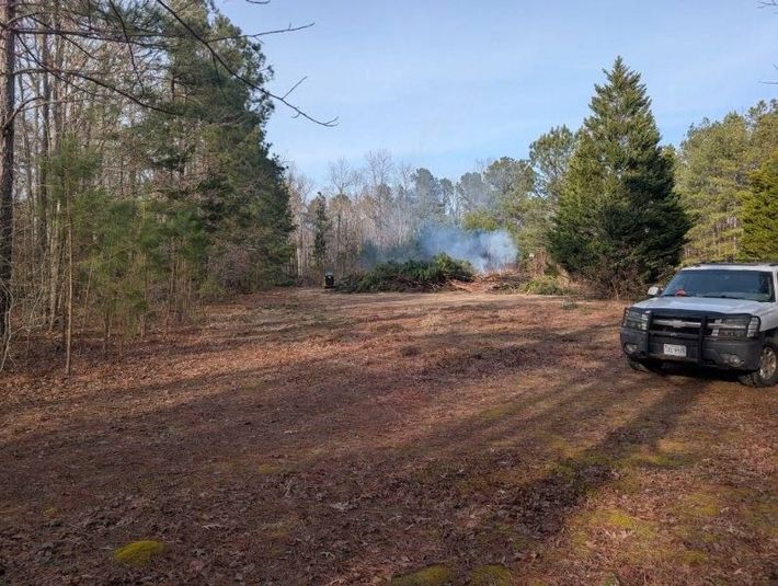 Rural dirt clearing with smoke in the distance and a black SUV parked on the right.