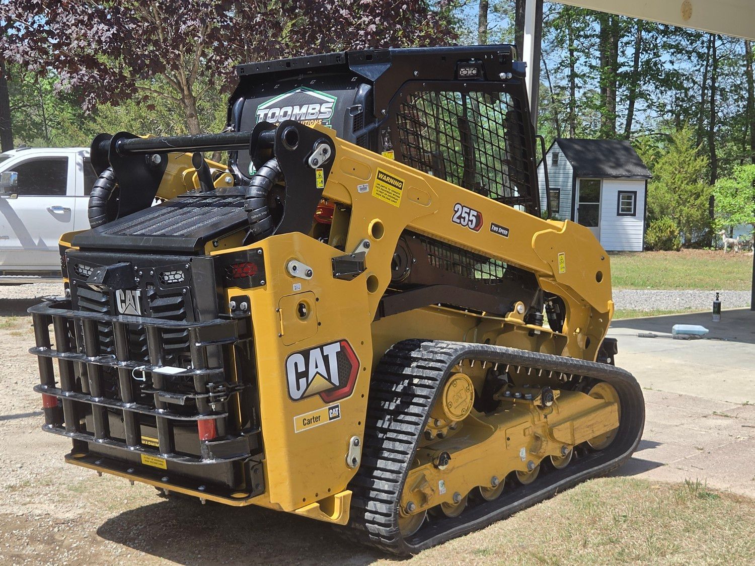 Yellow CAT track loader parked outdoors beside a road and trees