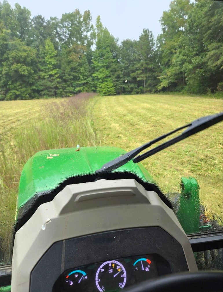 View from a green tractor driving through a mowed field toward a tree line