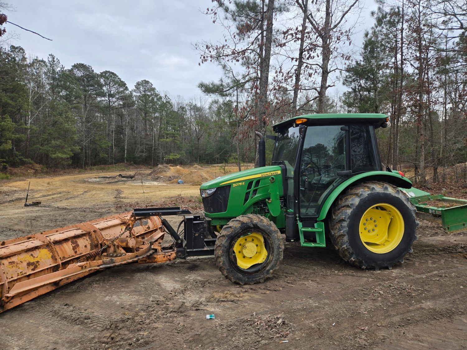 Green tractor with yellow wheels clearing debris in a muddy wooded area