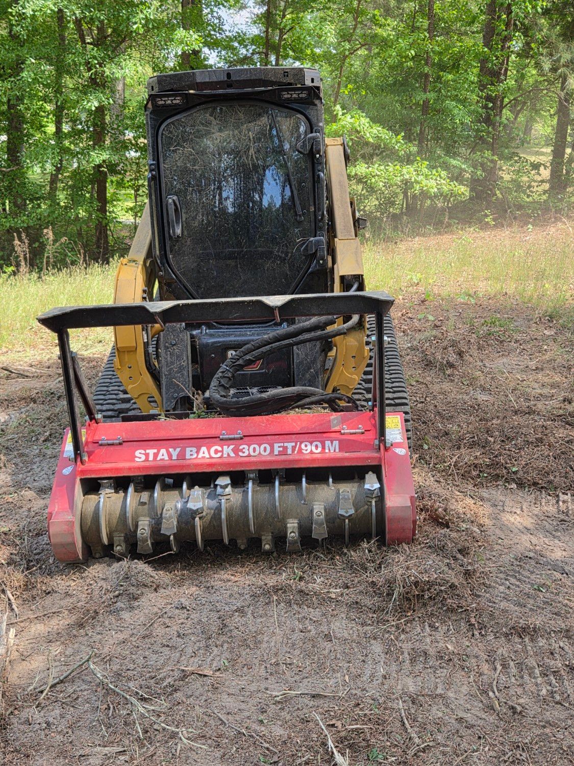 Red forestry mulcher attachment on a skid steer clearing brush in a wooded area