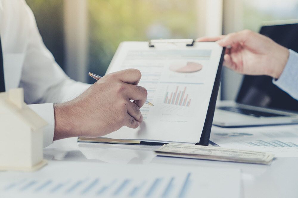 Two People Reviewing Documents at A Desk with A Small House Model, Financial Charts, and A Laptop — SDM Accounting & Taxation Services In Cooroy, QLD