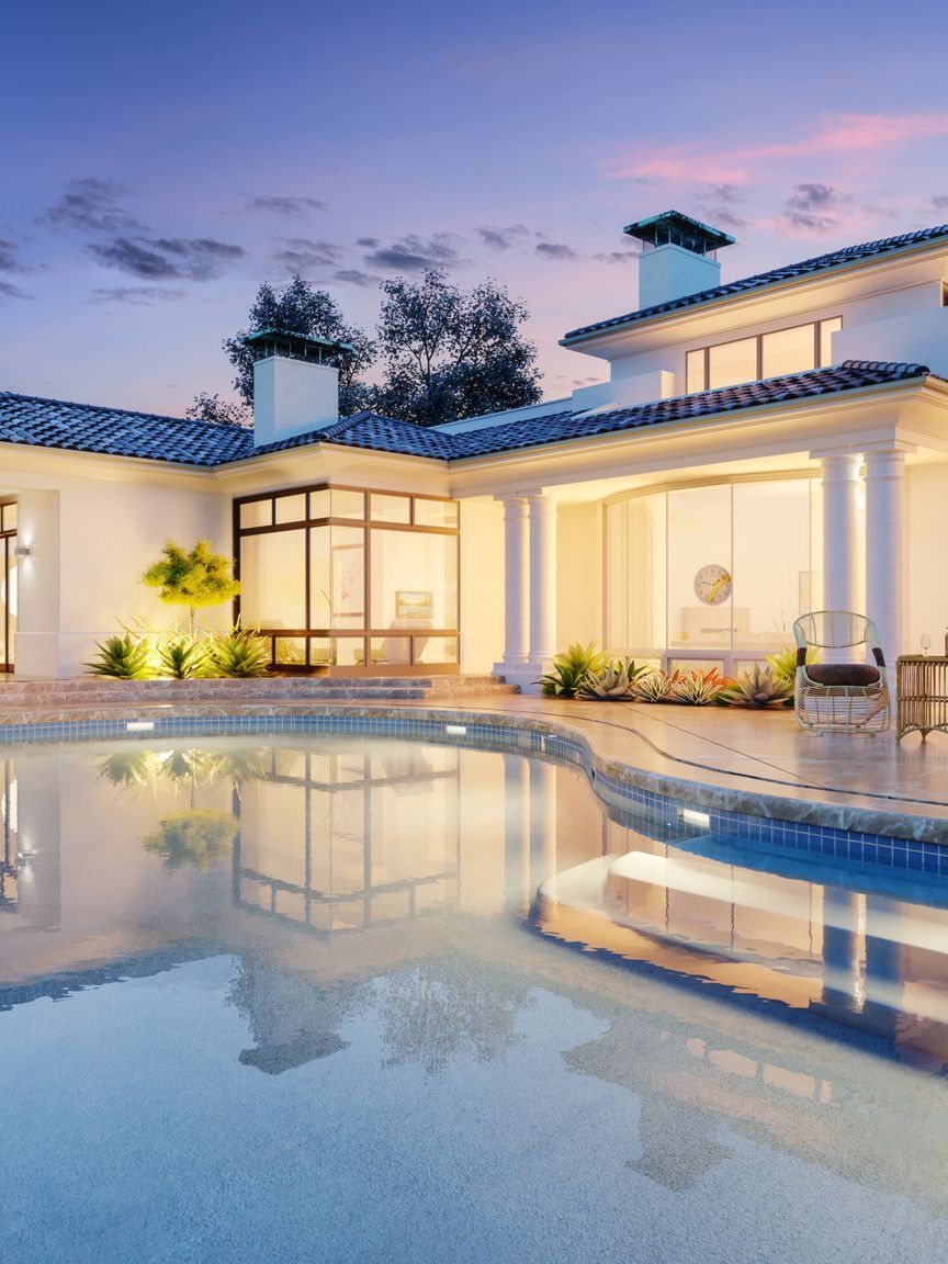 Luxury house with a lit pool at dusk, reflecting the home and blue evening sky