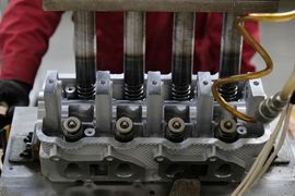 Engine cylinder head with four valves being assembled with an oil line attached.