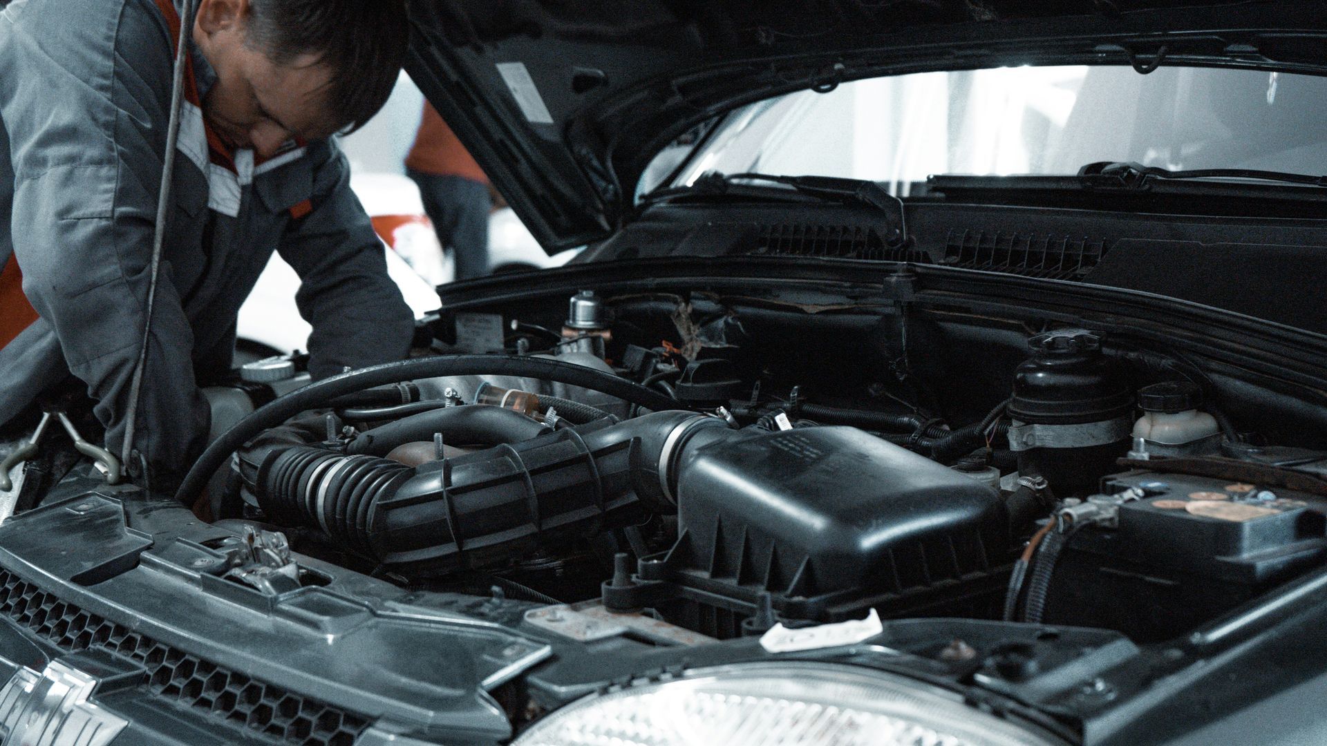Mechanic working on a car engine under the hood. Black car with open hood.