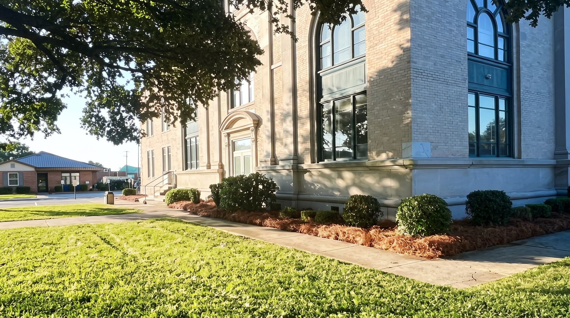 Stone church exterior with arched windows, landscaped shrubs, and a sunlit lawn