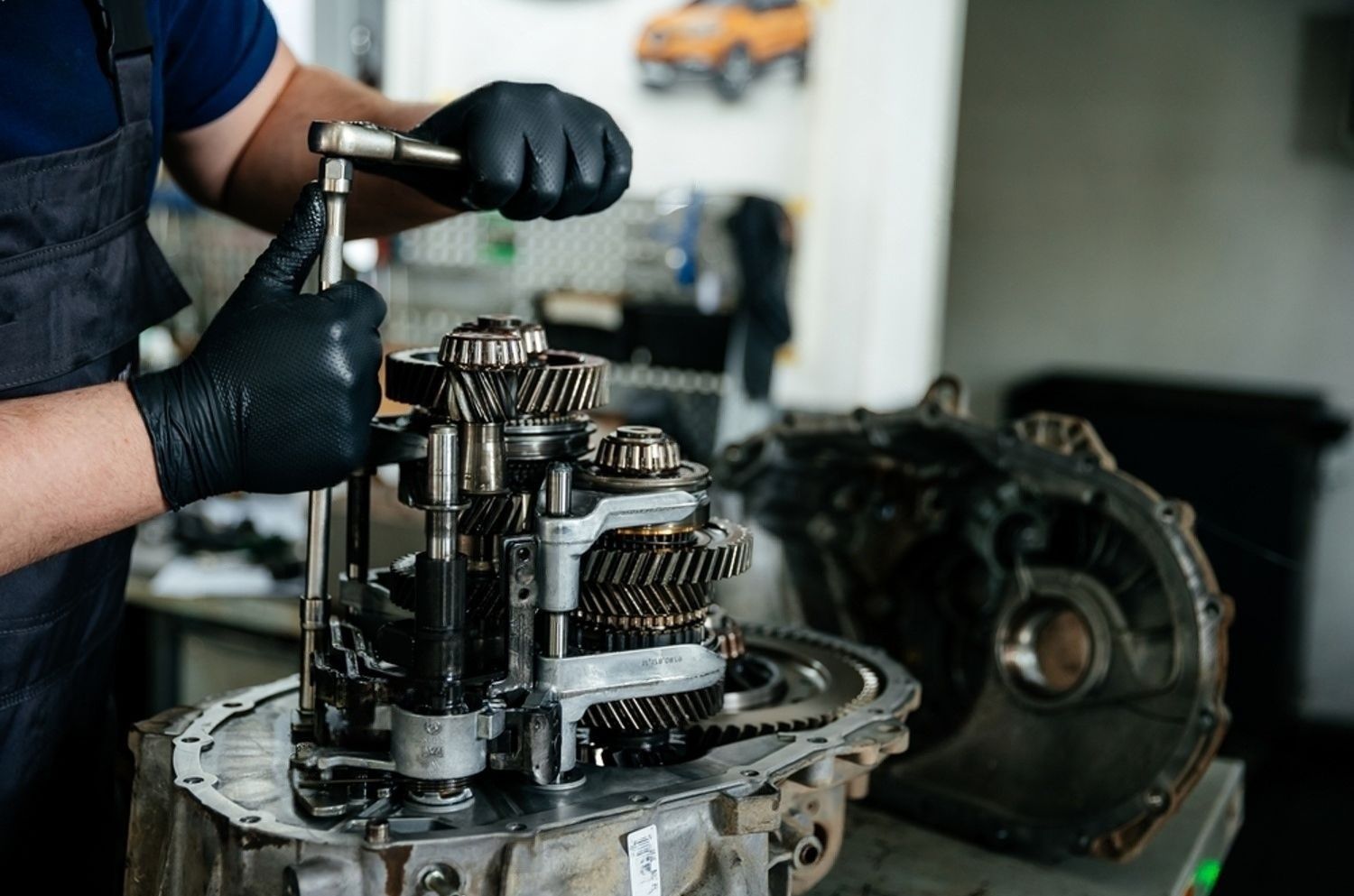 A man wearing black gloves is working on a gearbox in a garage.