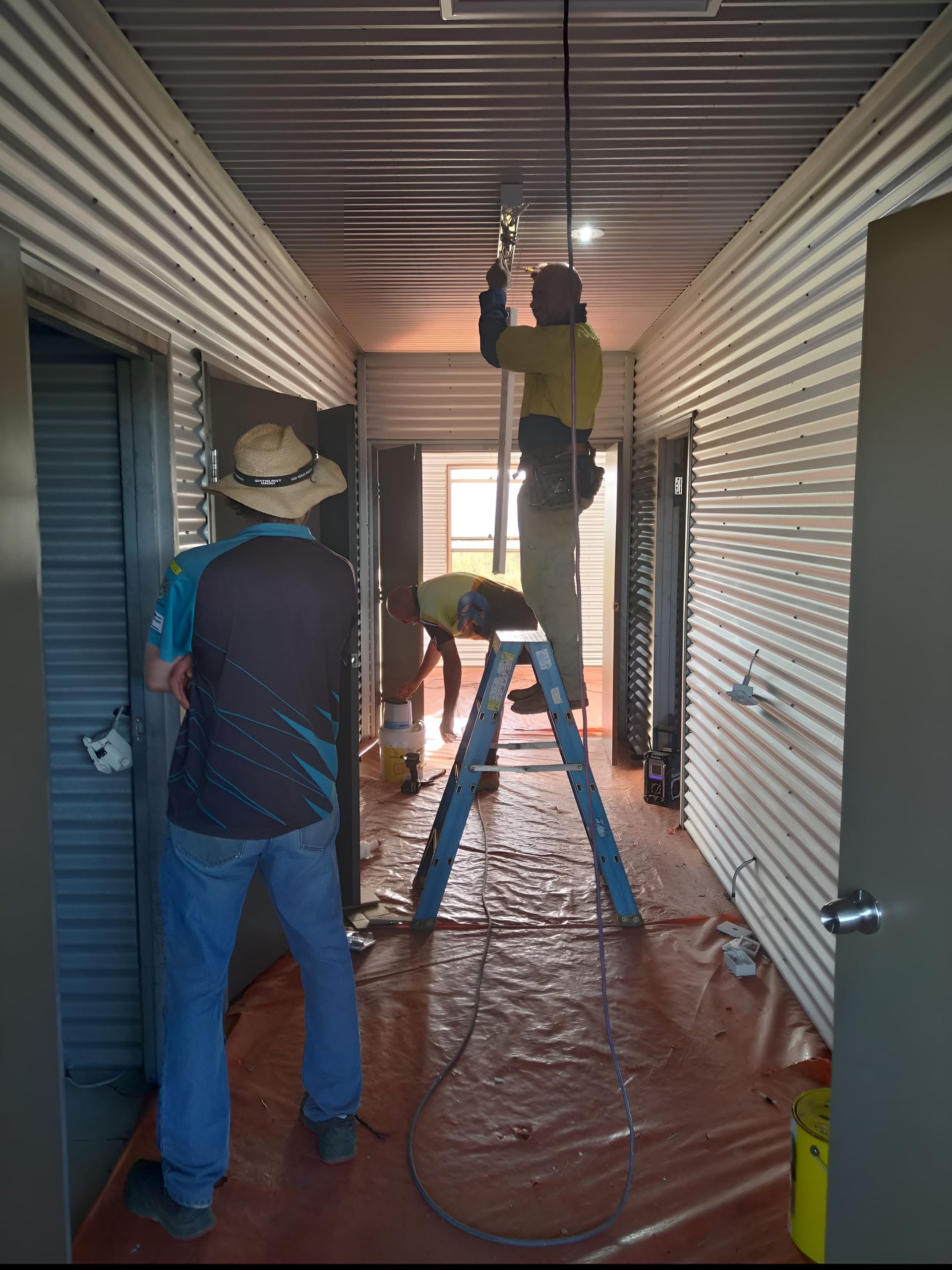 Men working in a corridor with one on a stepladder fixing a light — Alice Springs Electrical Services In Araluen, NT