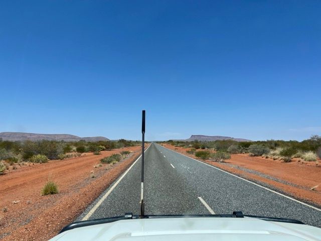 A car driving on a road with red dirt on either side — Alice Springs Electrical Services In Araluen, NT