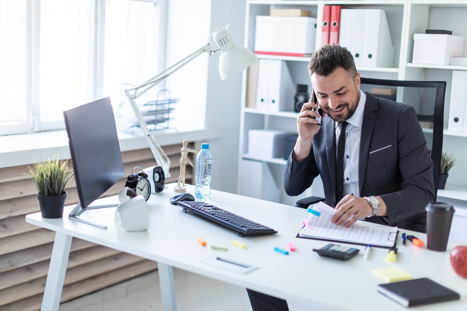 A man is sitting at a desk in an office talking on a cell phone.