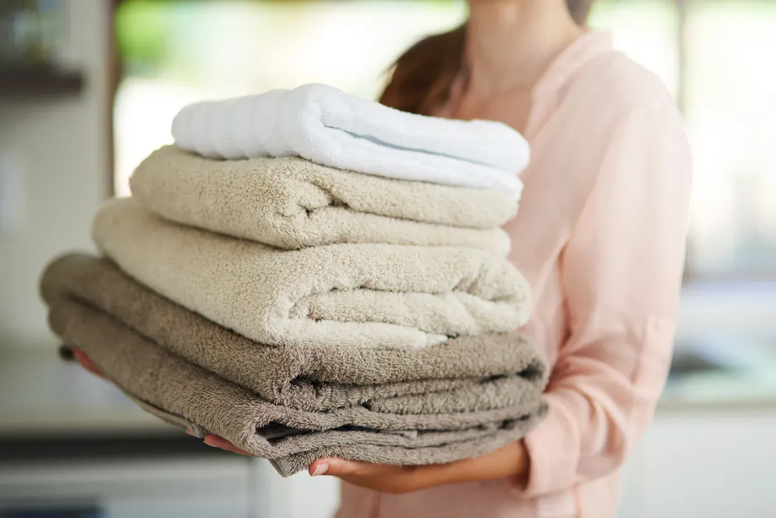 A woman is holding a stack of towels in her hands.