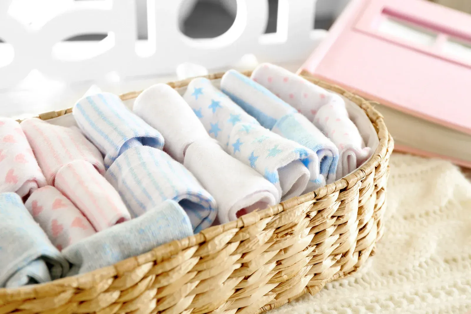 A wicker basket filled with a variety of baby clothes.