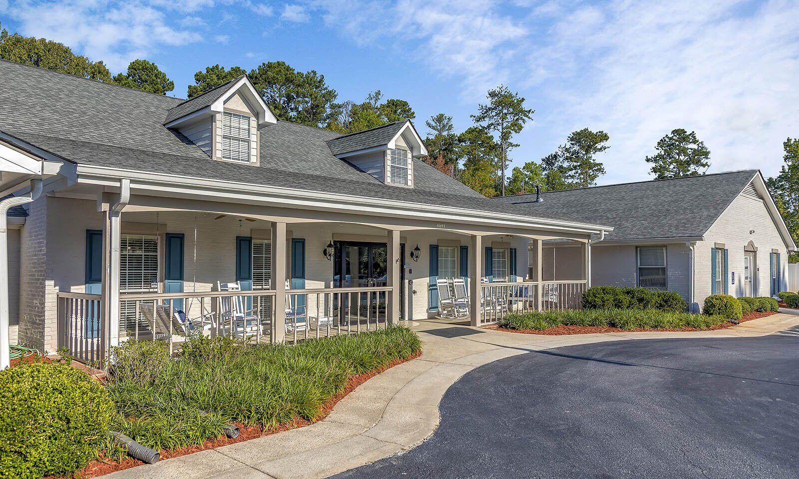 A large white house with a large porch and a driveway leading to it.
