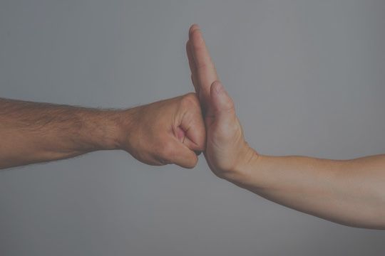 Fist bumping a flat palm, hands against gray backdrop.