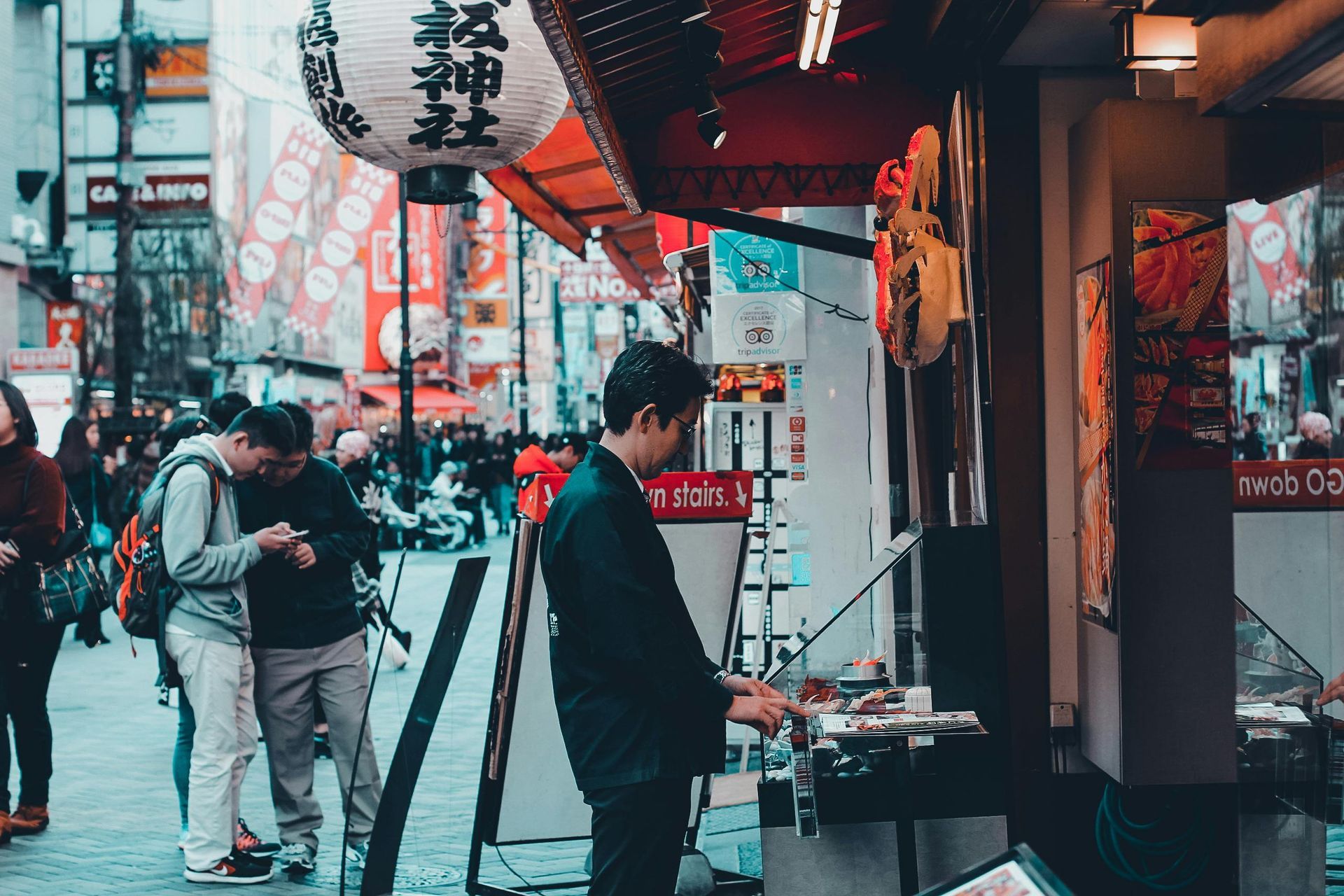 Man looking at items at a street shop in Japan; people in the background.