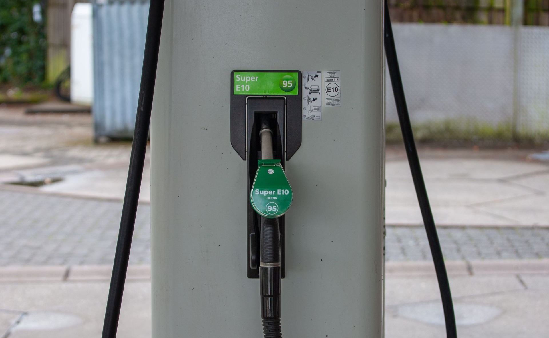 Green electric vehicle charger mounted on a gray pedestal at an outdoor station.