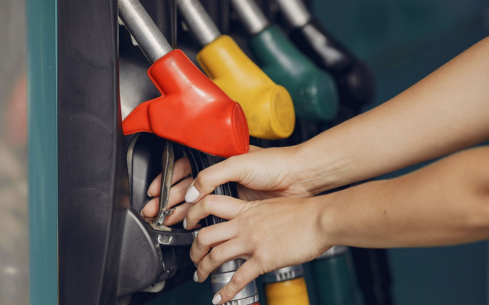 Hands at a gas pump, selecting red, yellow, and green fuel nozzles.