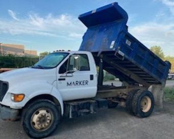 White dump truck with a blue bed, tilted up, parked outdoors.
