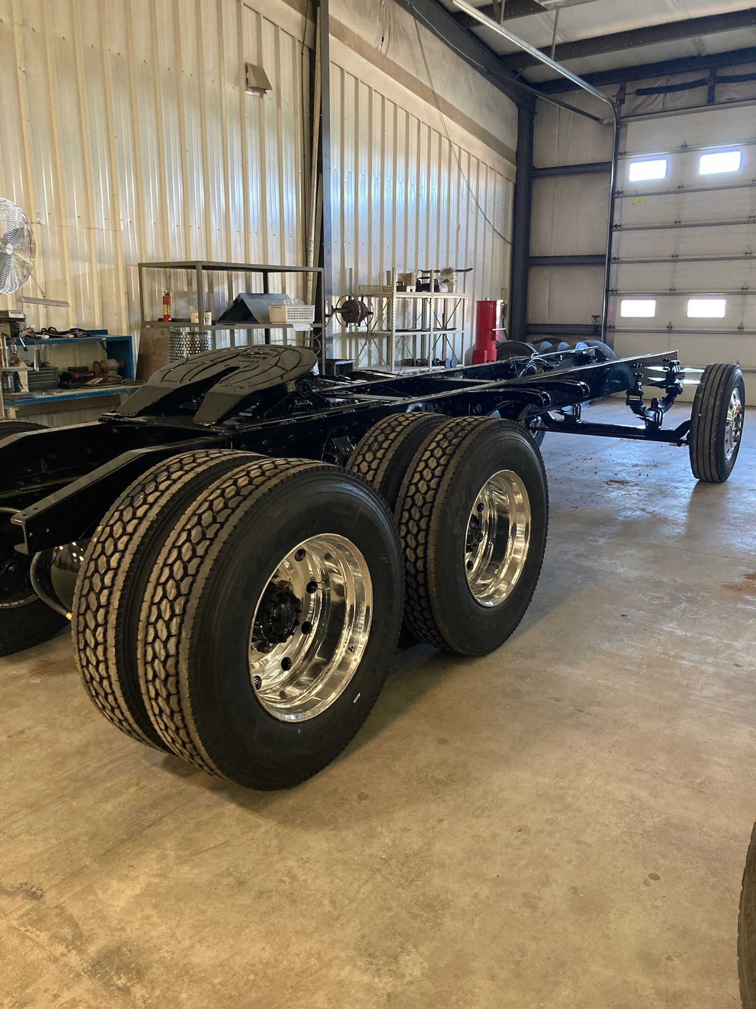 Black truck chassis with shiny wheels inside a warehouse.