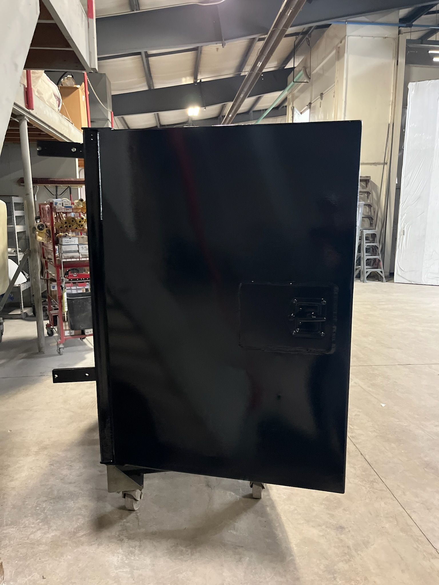 Black rectangular metal box on wheels in a factory setting.