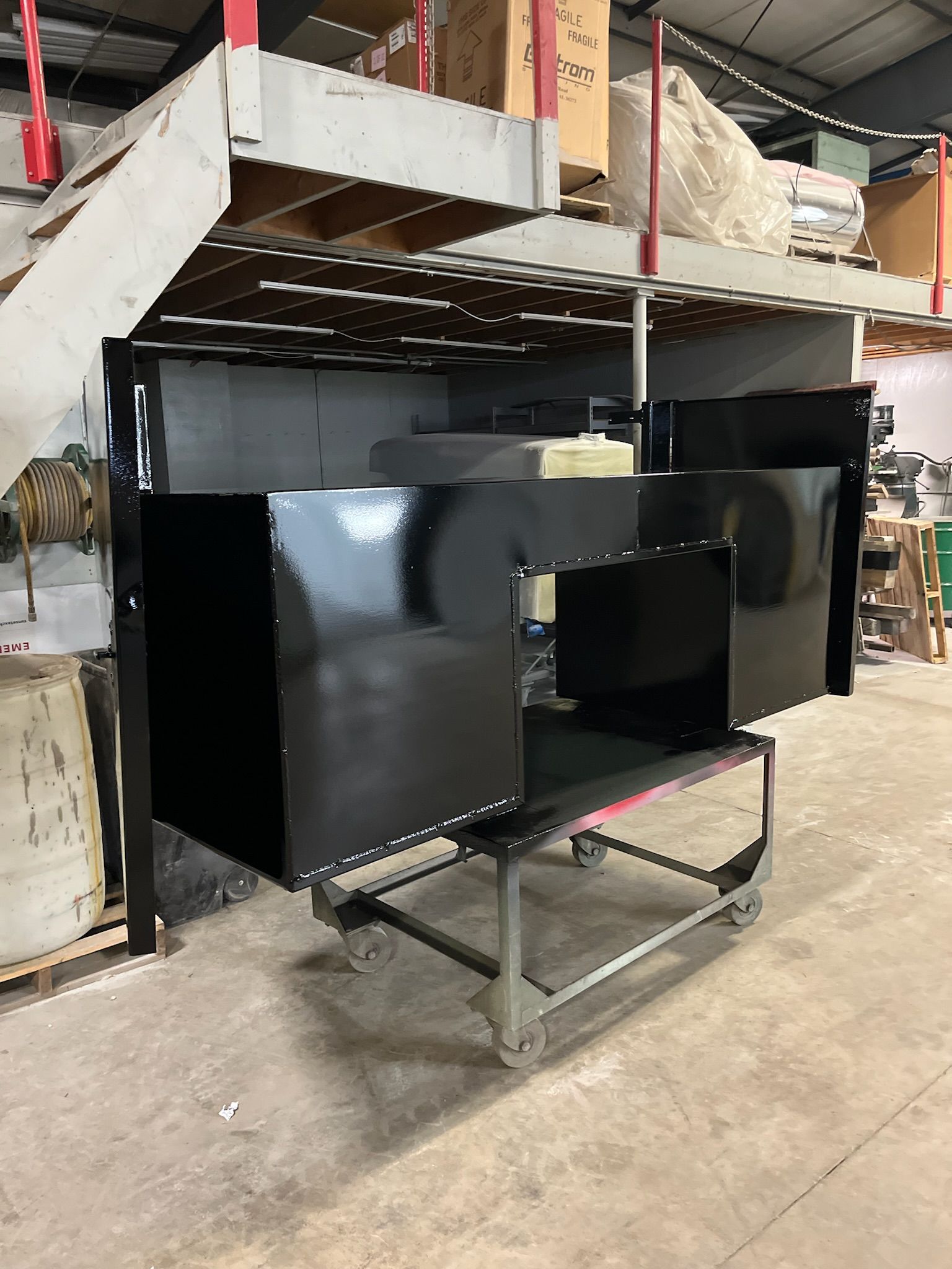Black metal enclosure on wheels in a warehouse setting, with a raised platform in the background.