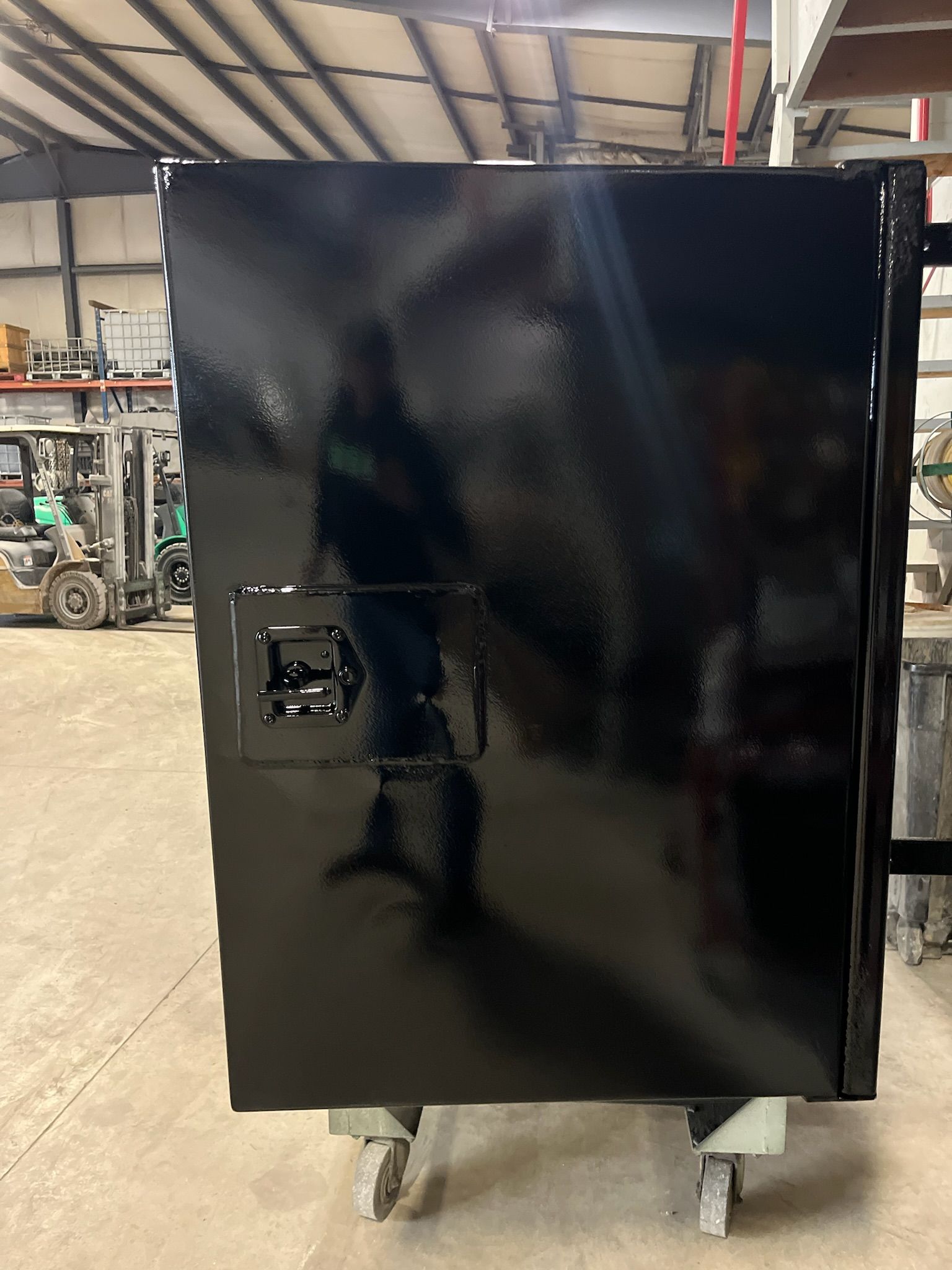 Black painted metal storage cabinet with a handle, on wheels, inside a warehouse.
